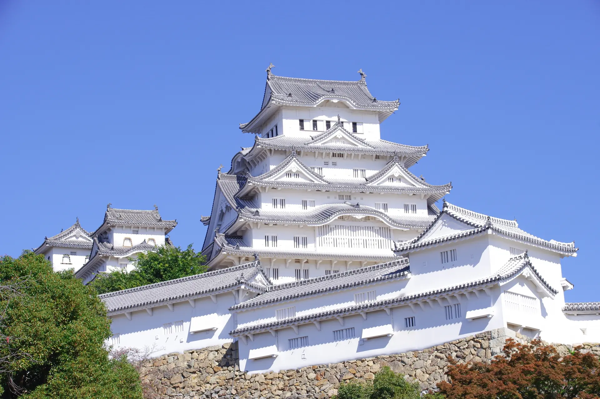 Himeji Castle, a magnificent white Japanese castle with tiered roofs, against a clear blue sky.