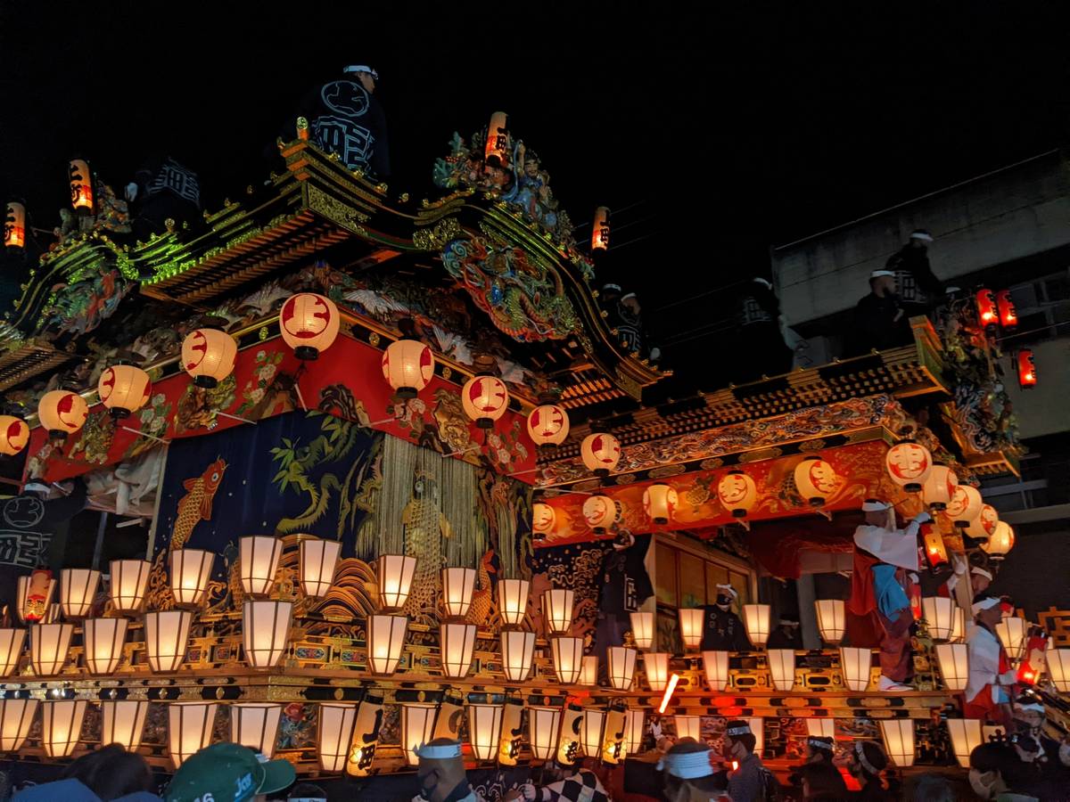 Ornate Japanese festival float illuminated by many lanterns at night, with people on and around it.