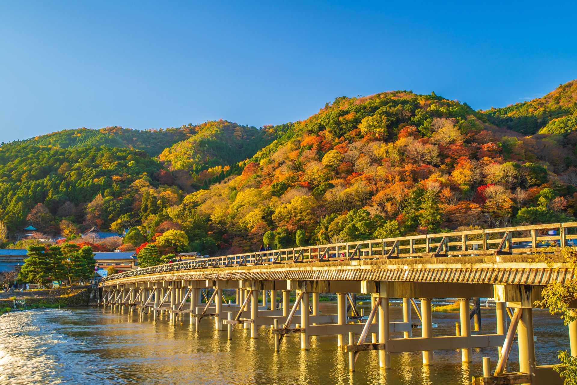 Wooden bridge spanning a river with hillsides vibrant with autumn foliage.