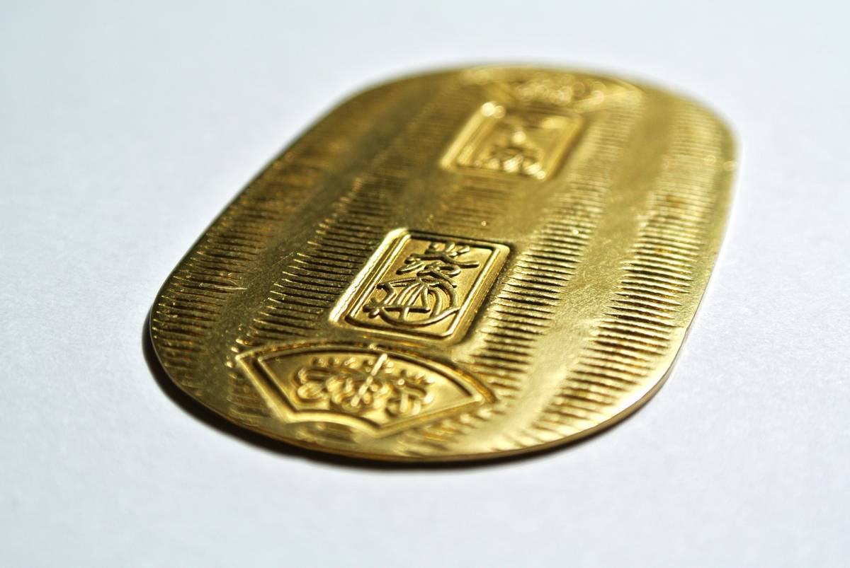 A gold oval Japanese oban coin with three embossed symbols and a ribbed texture.