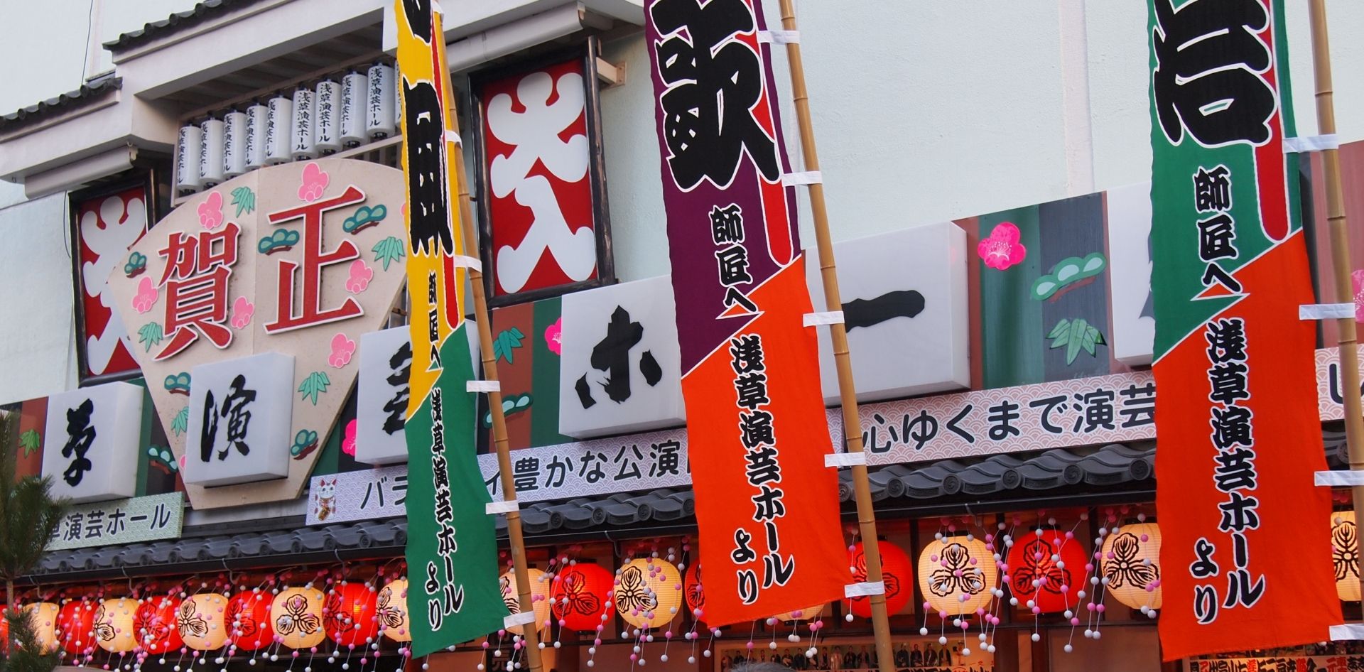 A festive Japanese entertainment hall decorated with colorful banners, New Year's signs, and glowing lanterns.