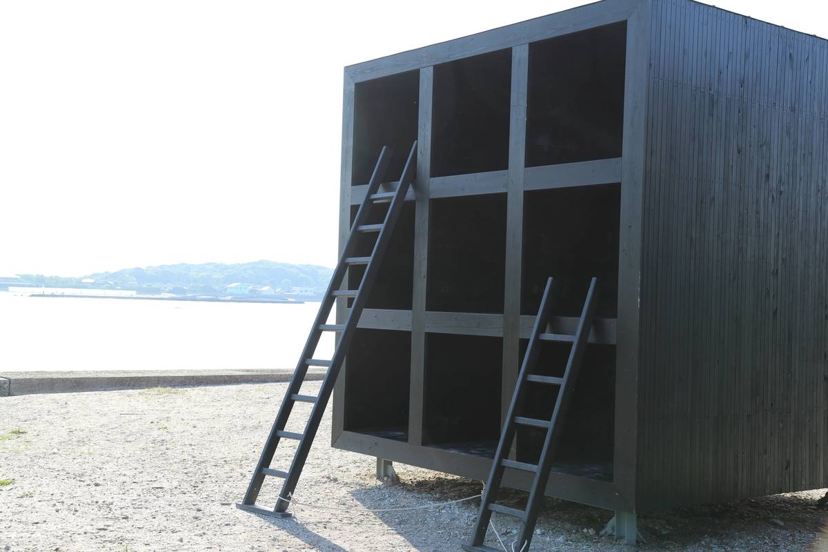 Dark wooden, multi-compartment structure with two ladders, by a sunny waterfront.