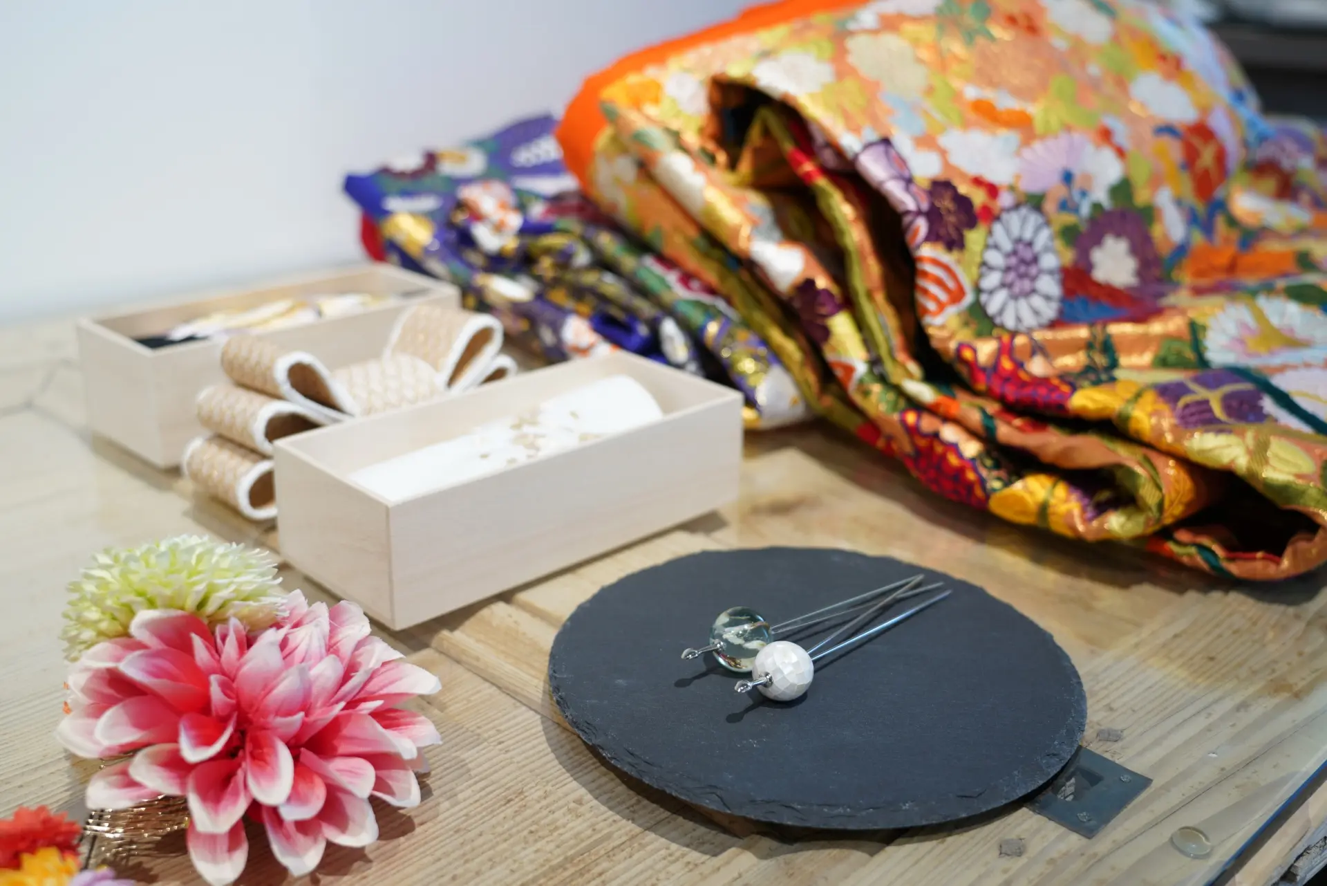 Colorful kimono fabric, decorative hairpins, and flowers arranged on a wooden table.