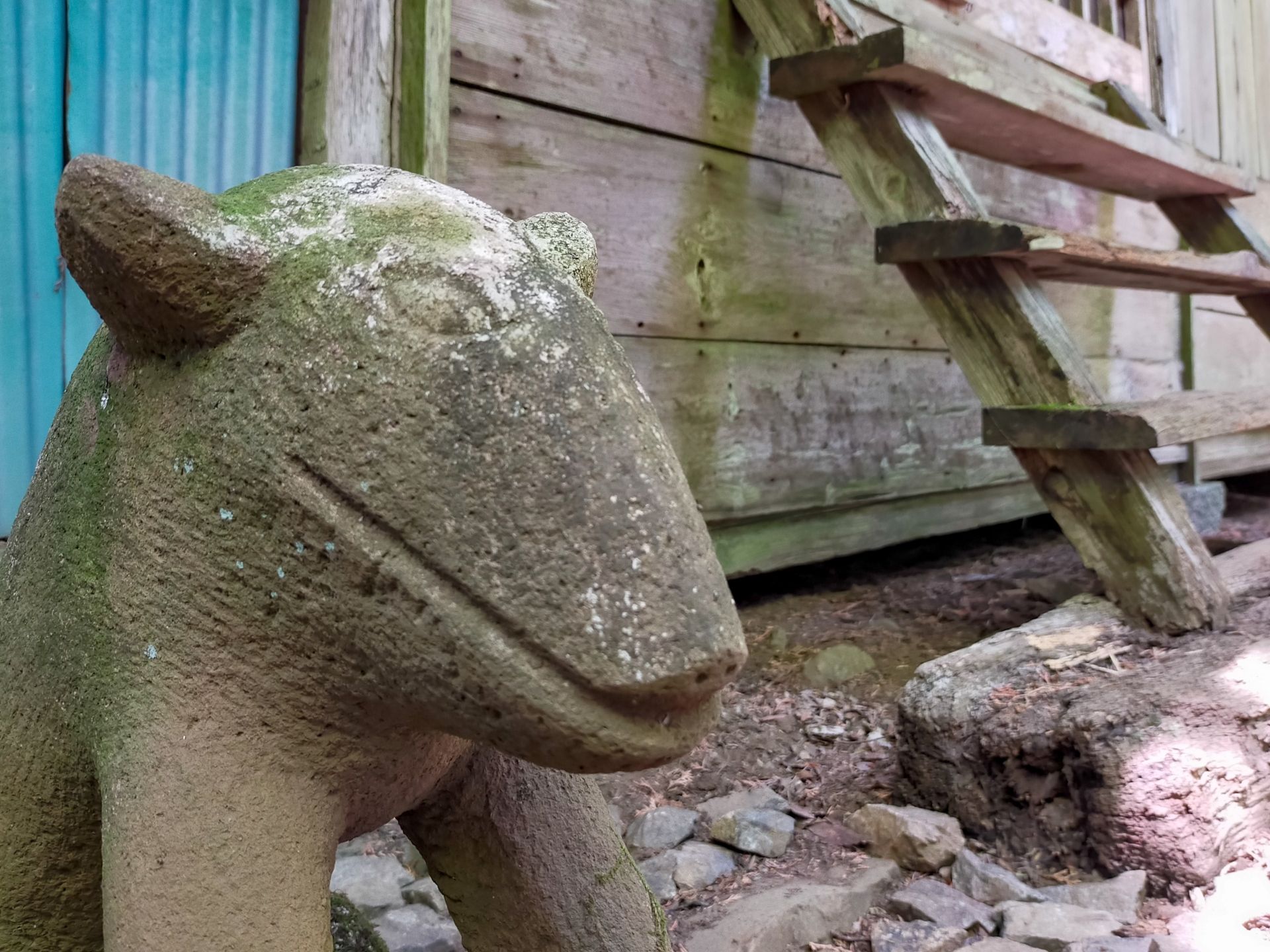 A moss-covered stone animal statue stands in front of a rustic wooden building with wooden steps.
