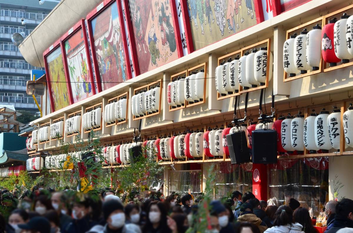A large crowd gathered beneath rows of Japanese lanterns and traditional art panels.