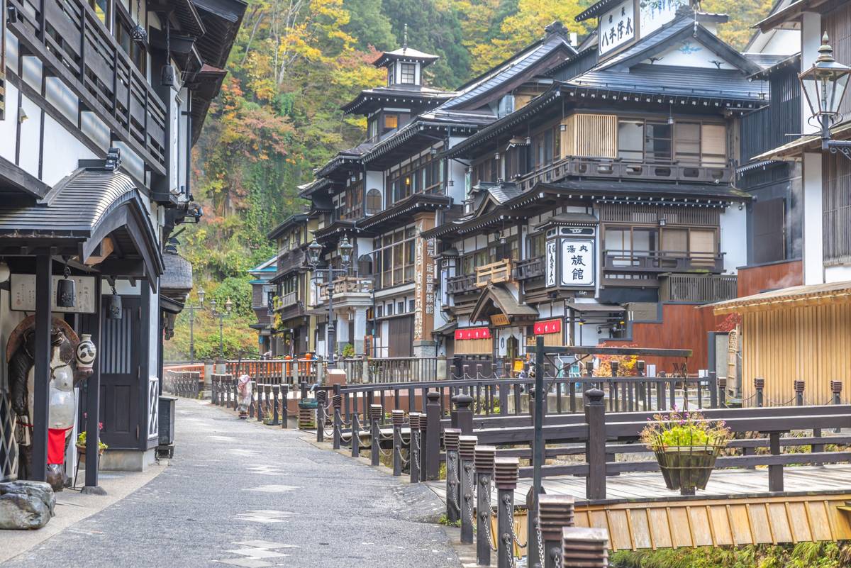 A traditional Japanese ryokan street with wooden buildings, a paved path, and autumn foliage.