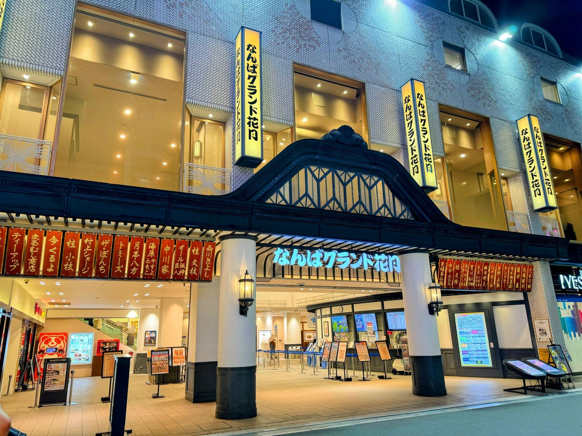 Illuminated entrance of Namba Grand Kagetsu theater at night, featuring Japanese signs, red banners, and an ornate archway.