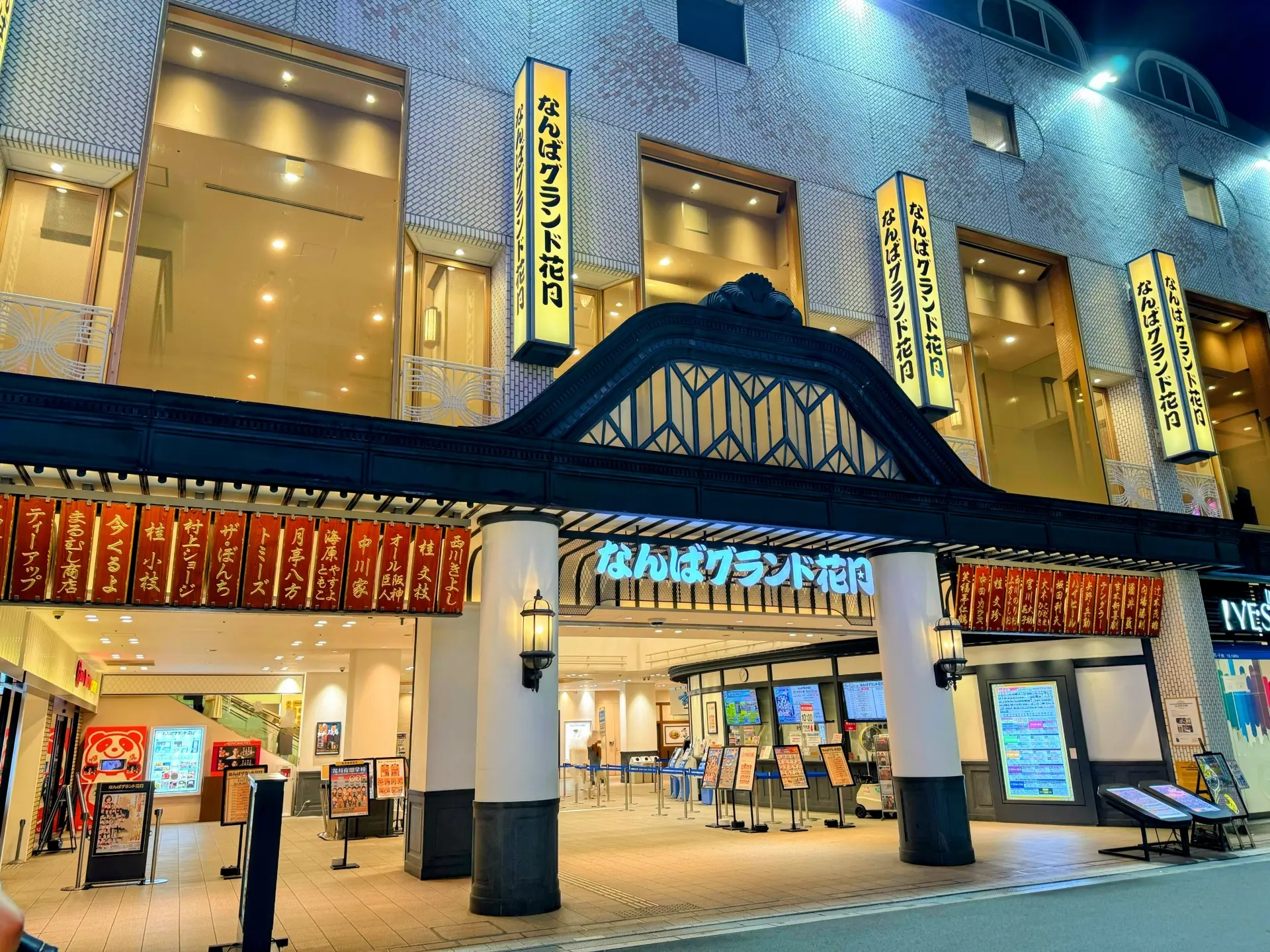 Illuminated entrance of Namba Grand Kagetsu theater at night, featuring Japanese signs, red banners, and an ornate archway.