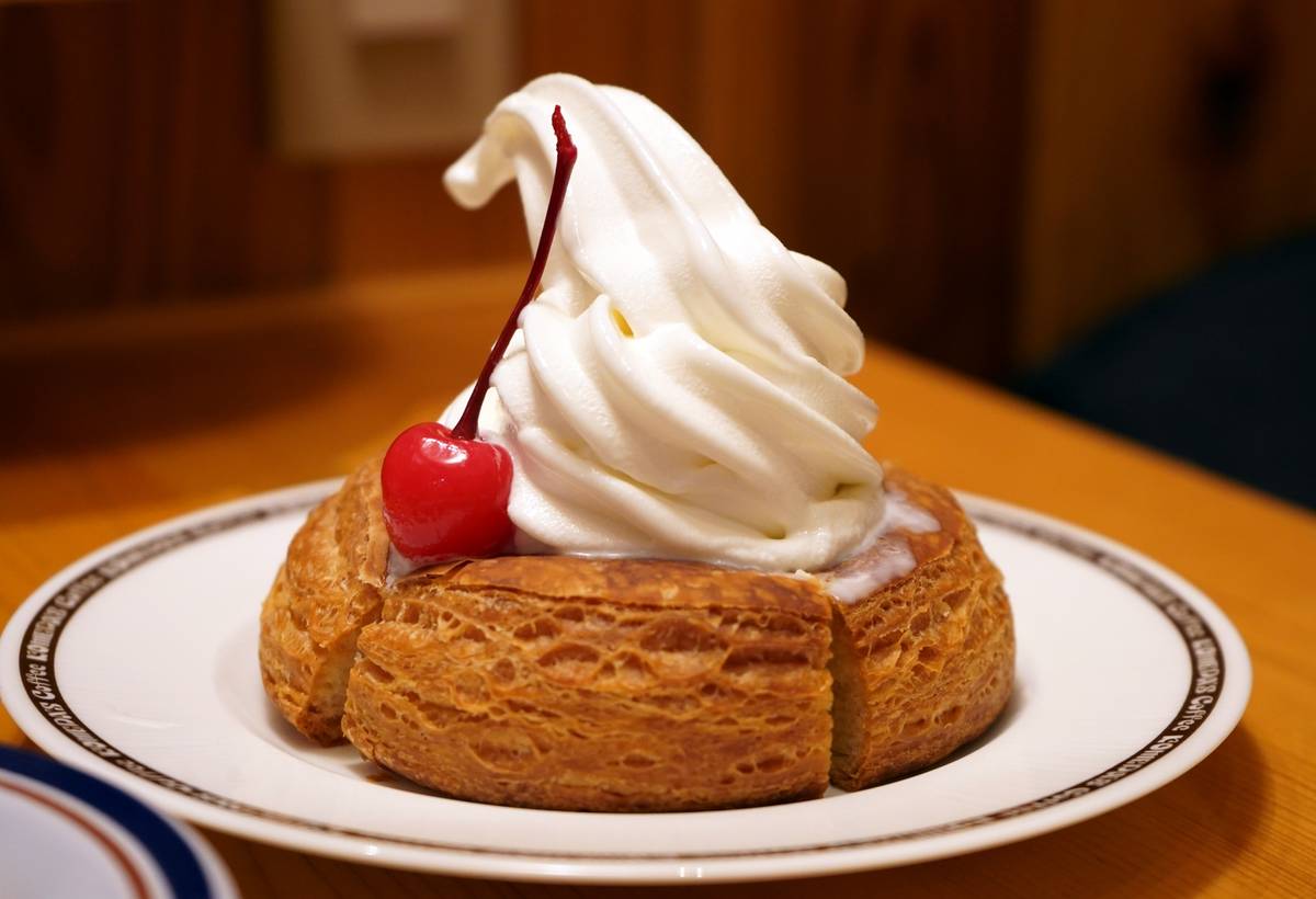 A golden-brown pastry topped with white soft-serve and a red cherry on a white plate.