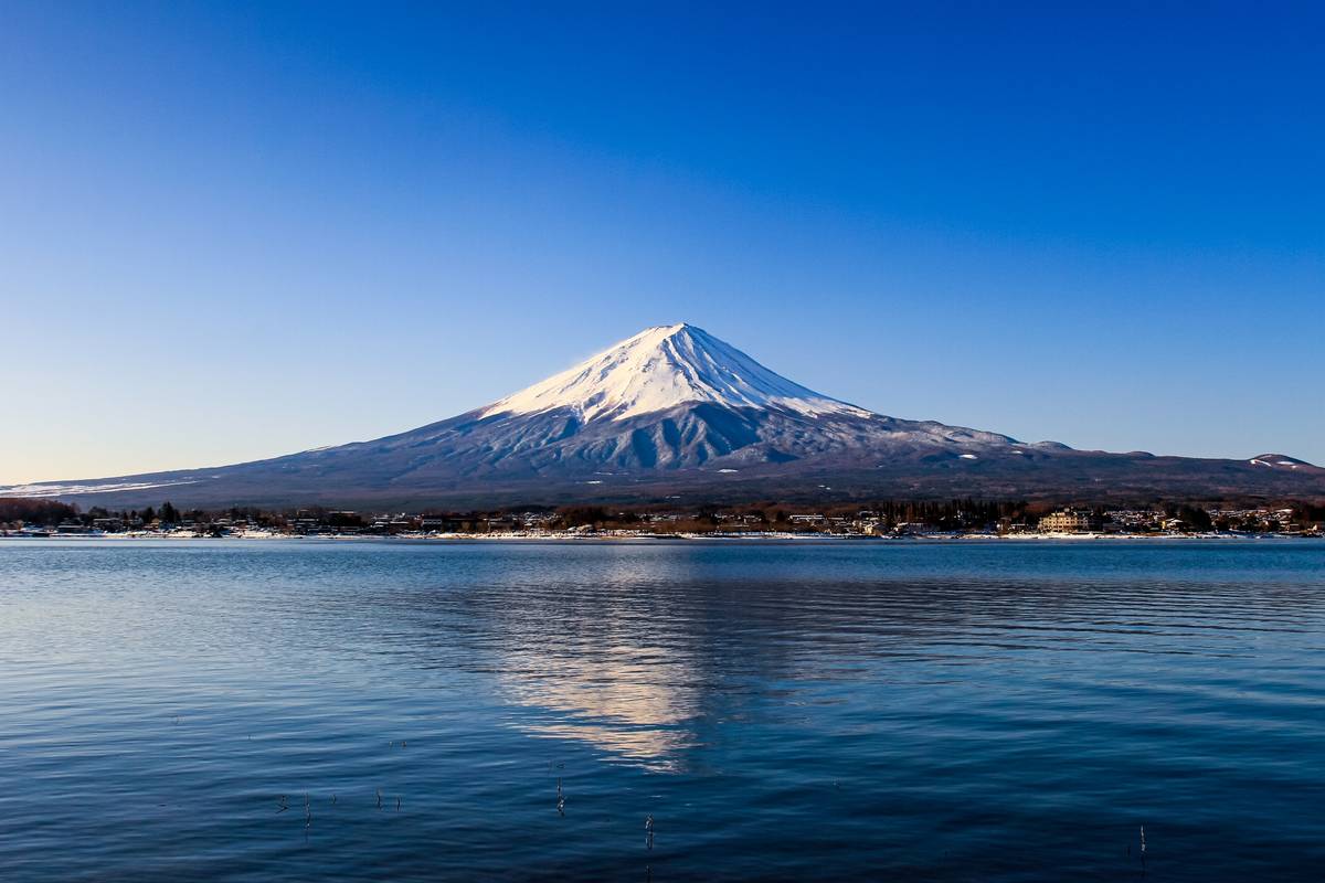 Snow-capped Mount Fuji reflects in a lake under a clear blue sky.