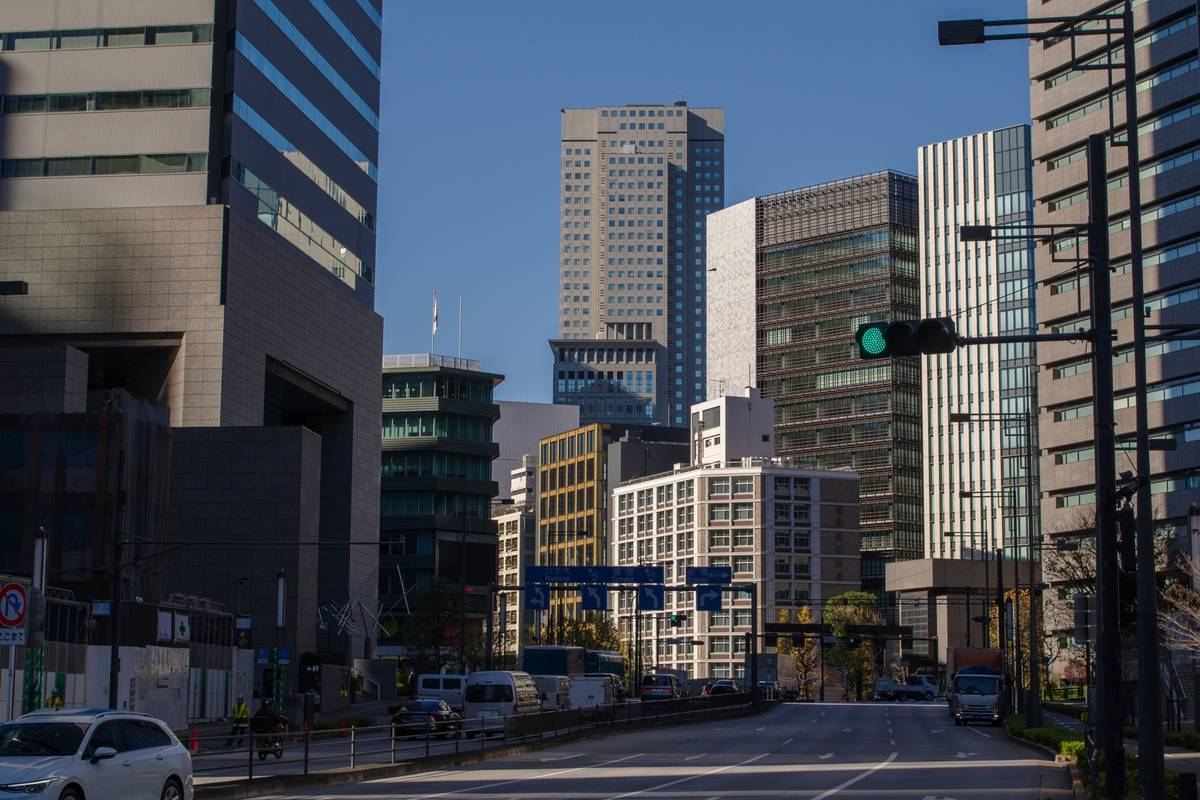 A city street with modern skyscrapers under a clear blue sky, featuring a green traffic light and moving traffic.