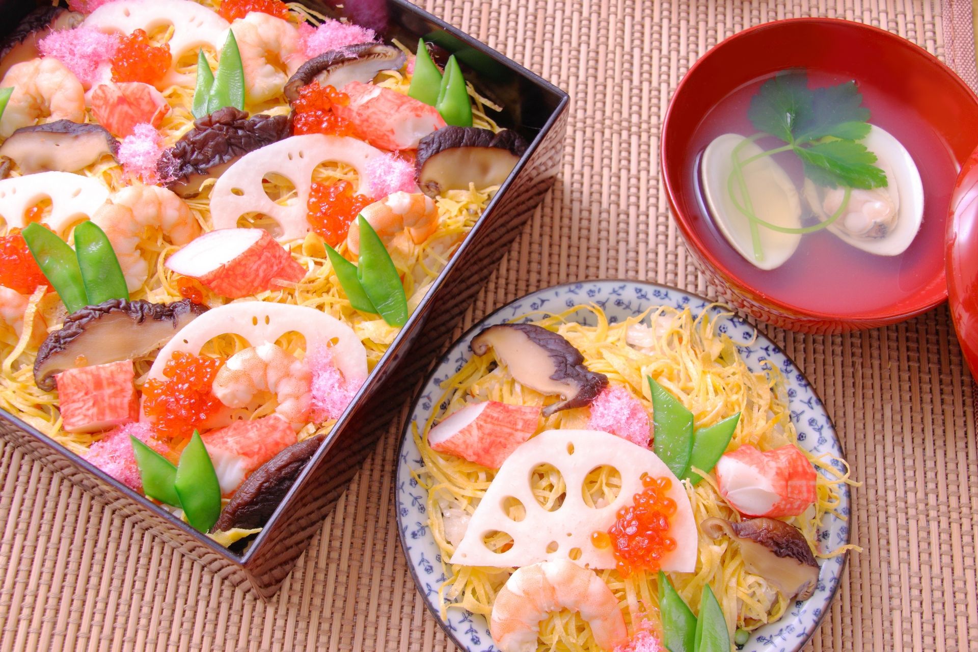 Overhead of chirashi sushi with shrimp, crab, lotus root, and roe, presented in a bento box and a plate