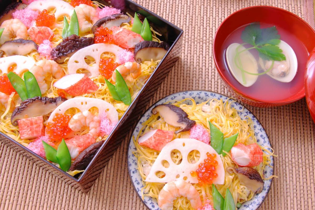 Overhead of chirashi sushi with shrimp, crab, lotus root, and roe, presented in a bento box and a plate