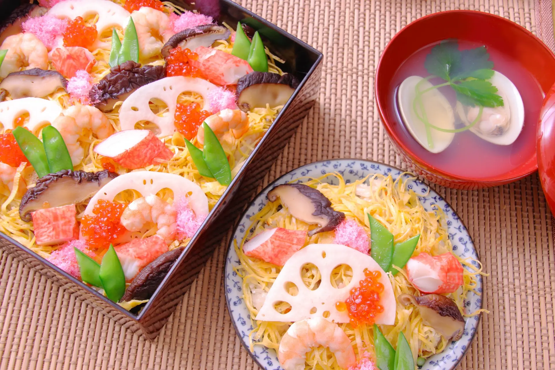 Overhead of chirashi sushi with shrimp, crab, lotus root, and roe, presented in a bento box and a plate