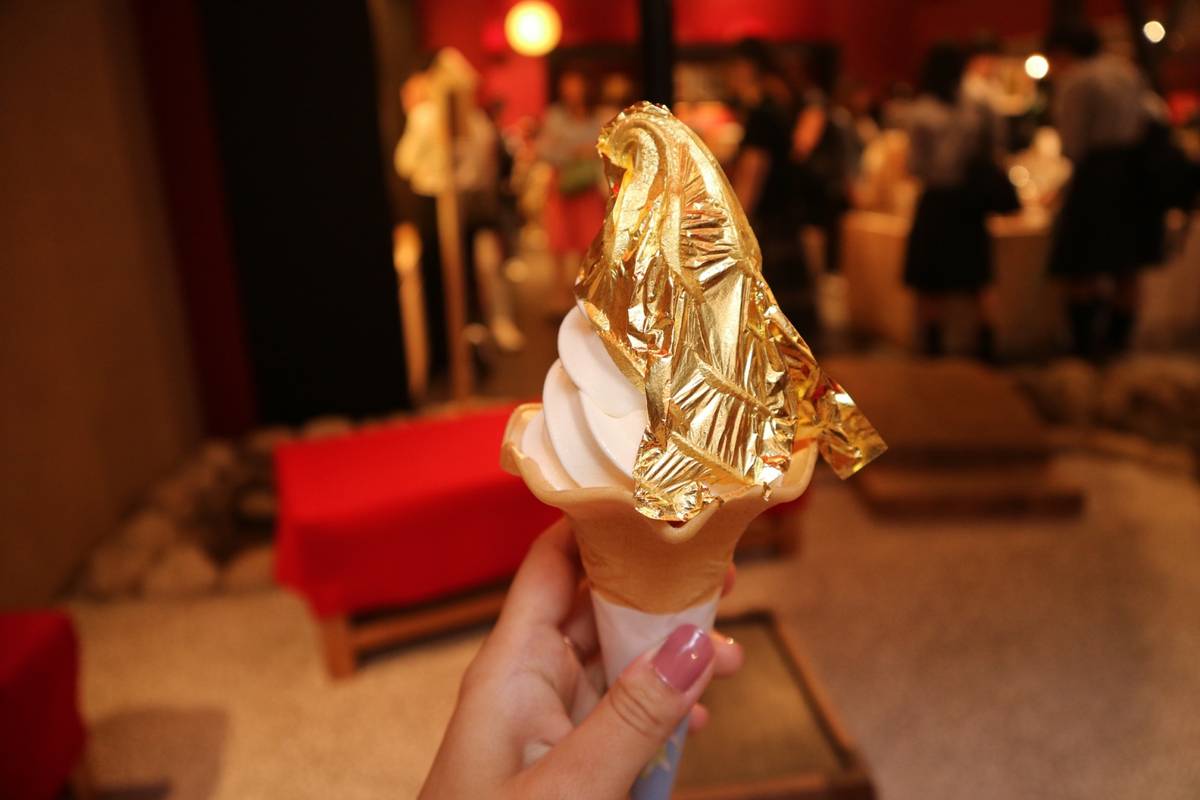 A hand holds a soft-serve ice cream cone adorned with gold leaf.