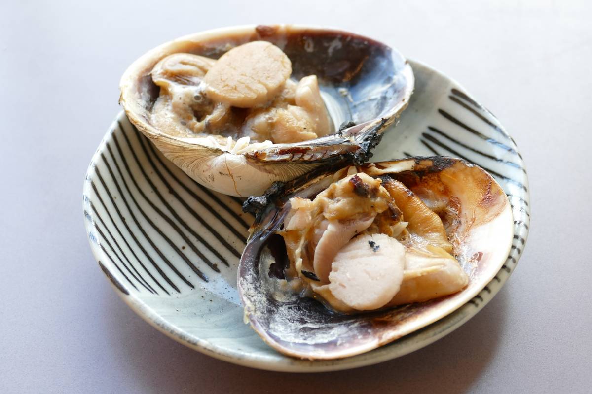 Two open clam shells filled with cooked scallops and other shellfish on a striped plate.