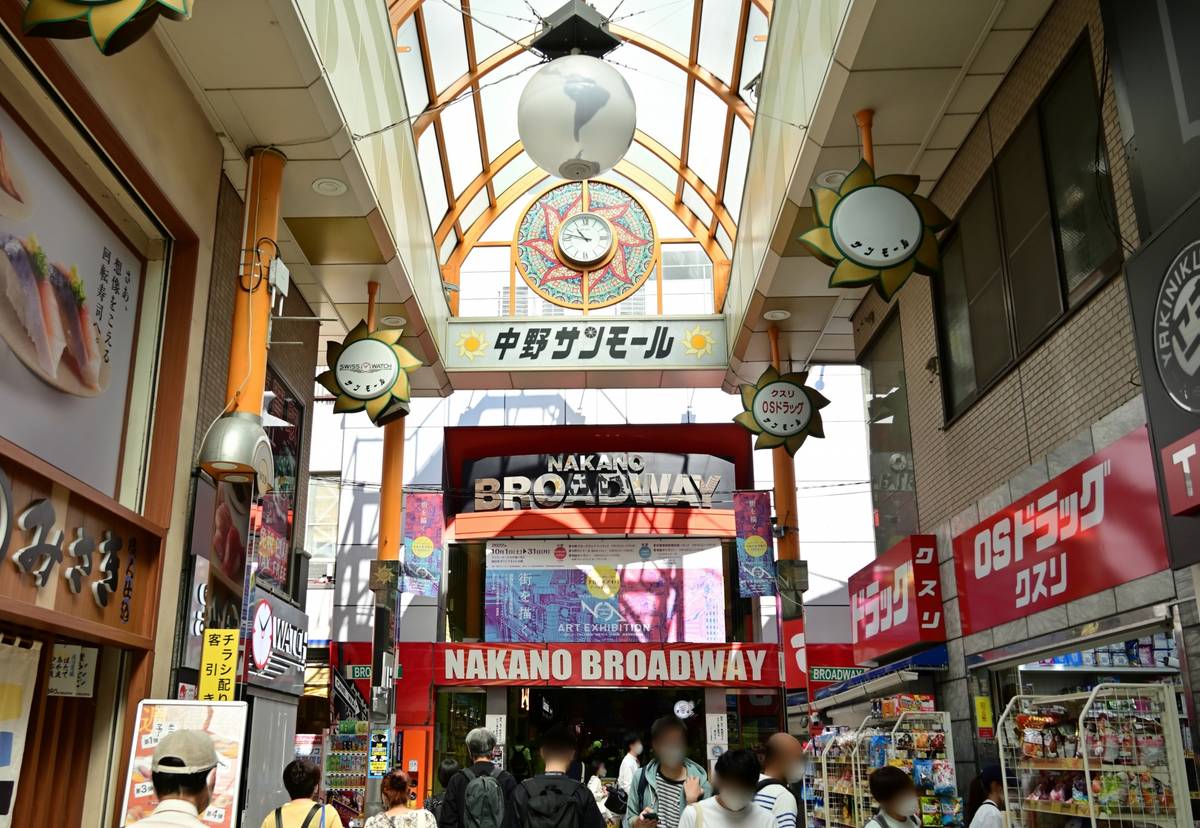 A bustling covered shopping arcade, Nakano Sun Mall, leading to the entrance of Nakano Broadway, with shops and people.
