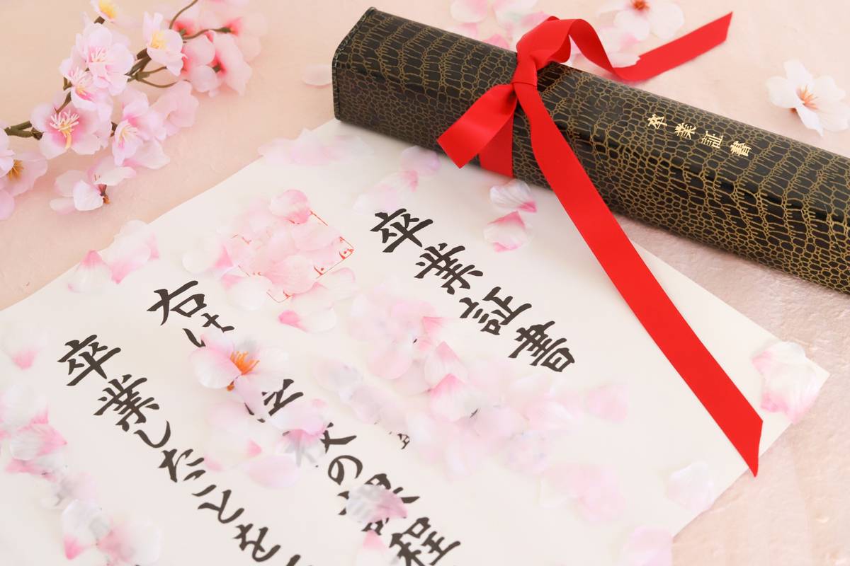 Japanese graduation diploma and scroll with red ribbon, adorned with cherry blossoms.