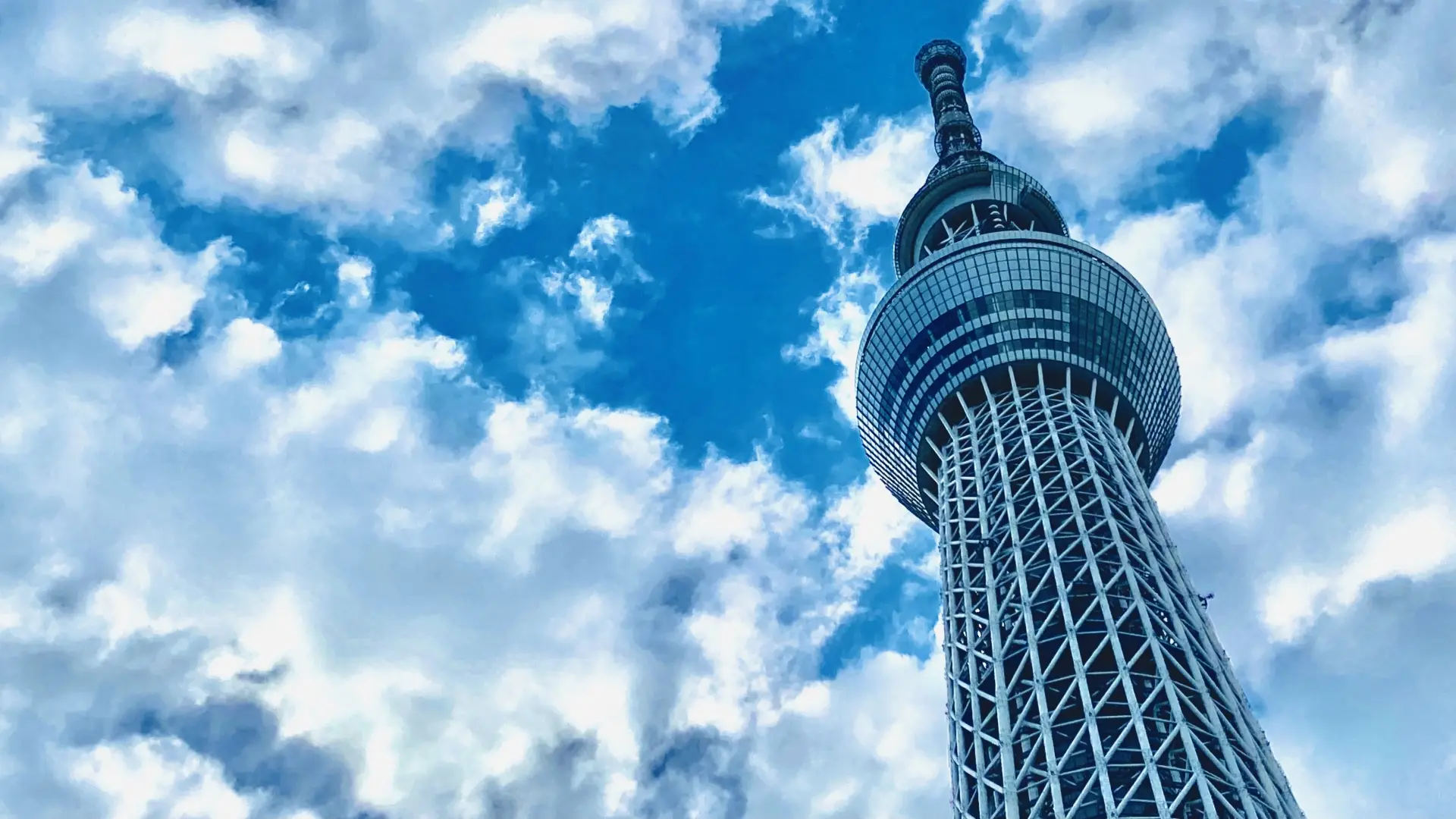 The Tokyo Skytree seen from below against a blue sky with white clouds.