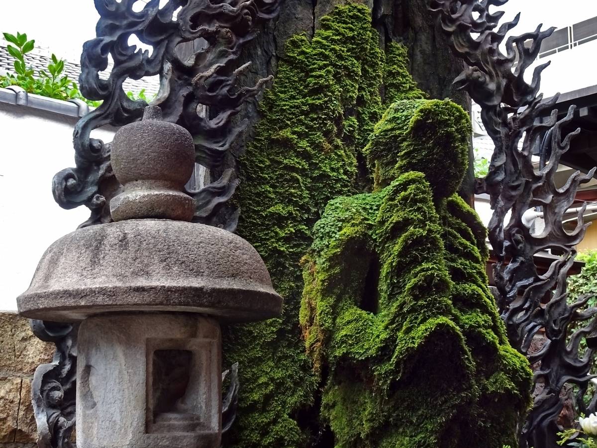 A stone lantern next to a moss-covered statue and dark, ornate carvings.