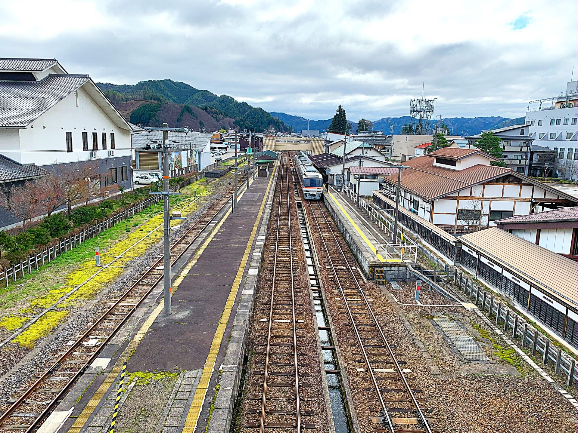 An aerial view of a train station with multiple tracks, platforms, a train at a platform, town buildings