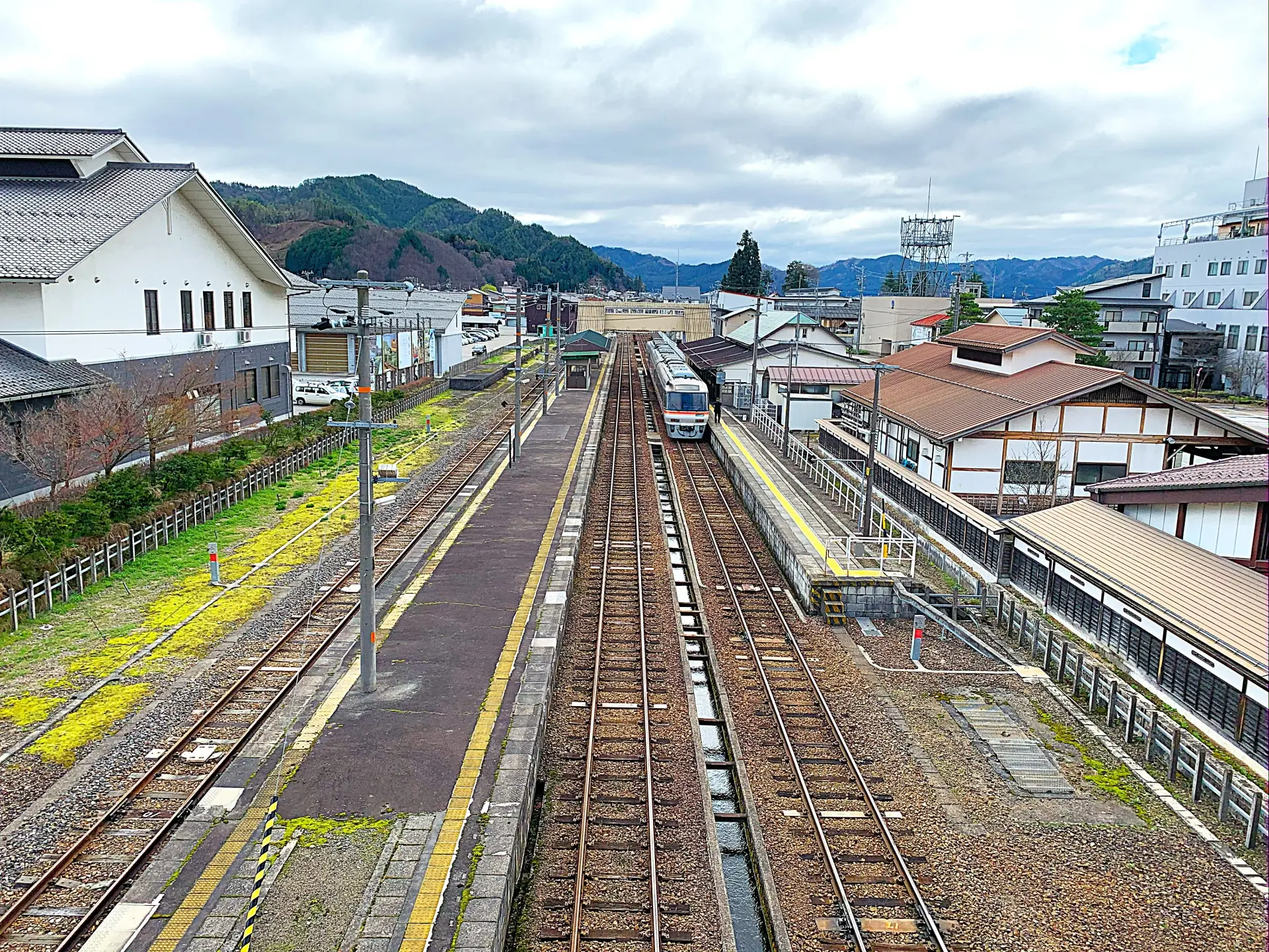 An aerial view of a train station with multiple tracks, platforms, a train at a platform, town buildings