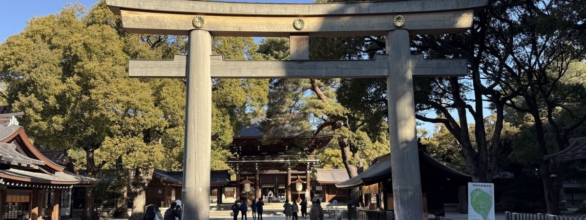 Large stone torii gate in front of a traditional Japanese shrine surrounded by trees.