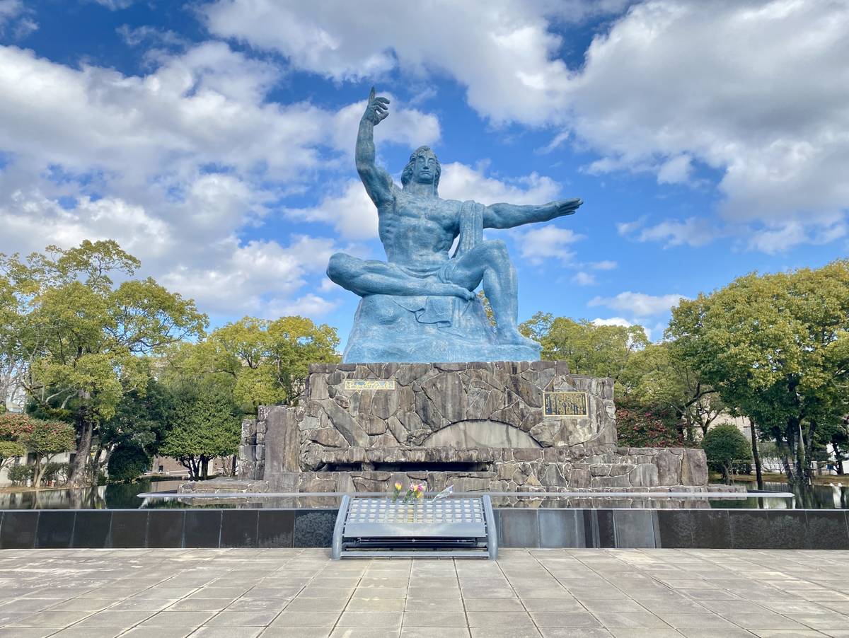 Nagasaki Peace Statue: A colossal blue man seated on a stone base, right arm pointing skyward, left arm extended