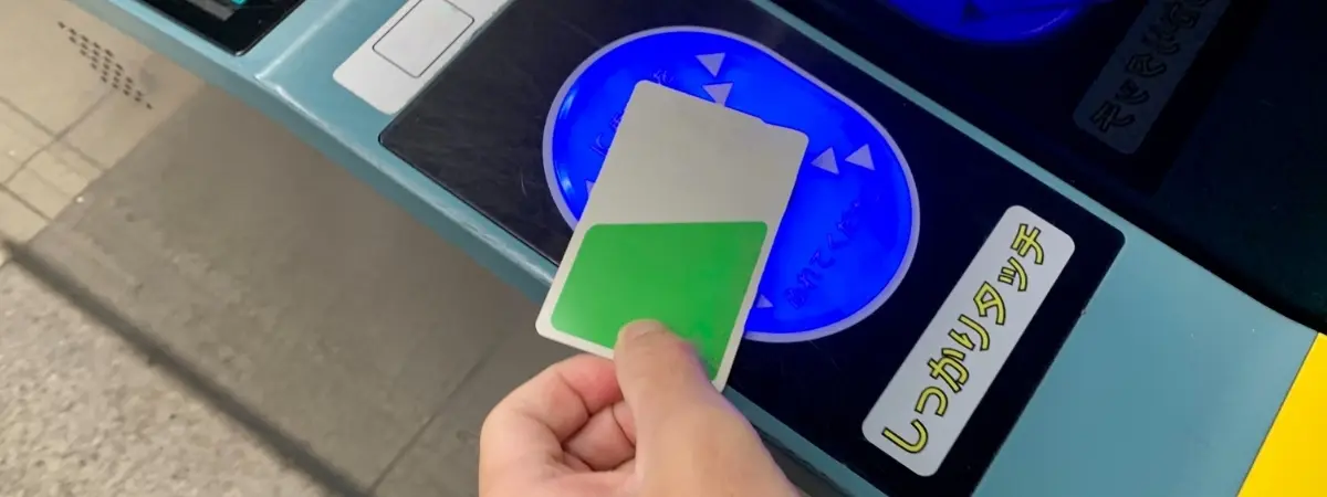 A hand holds a white card with a green rectangle over a blue glowing contactless card reader.