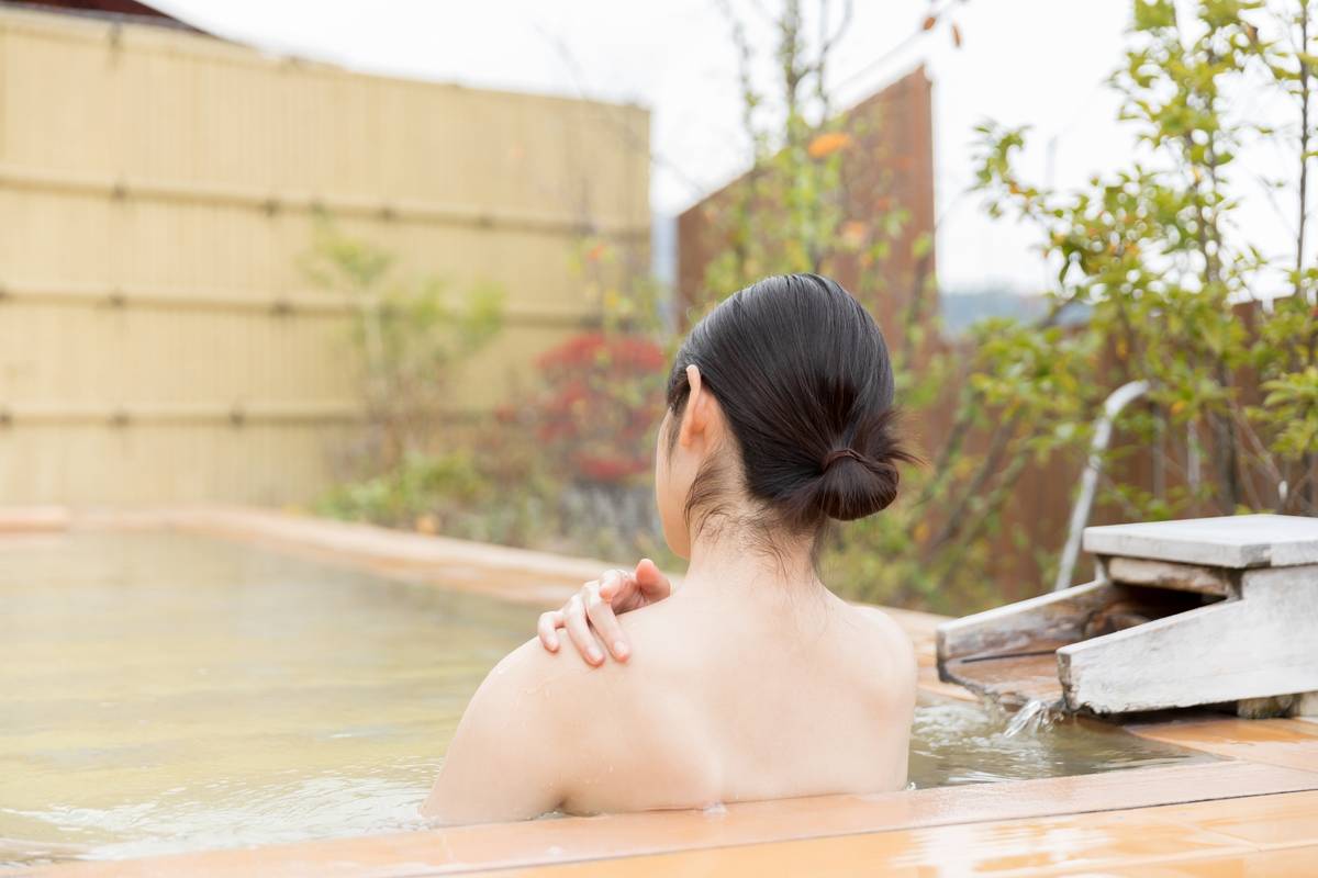 Woman from behind relaxing in an outdoor hot spring.