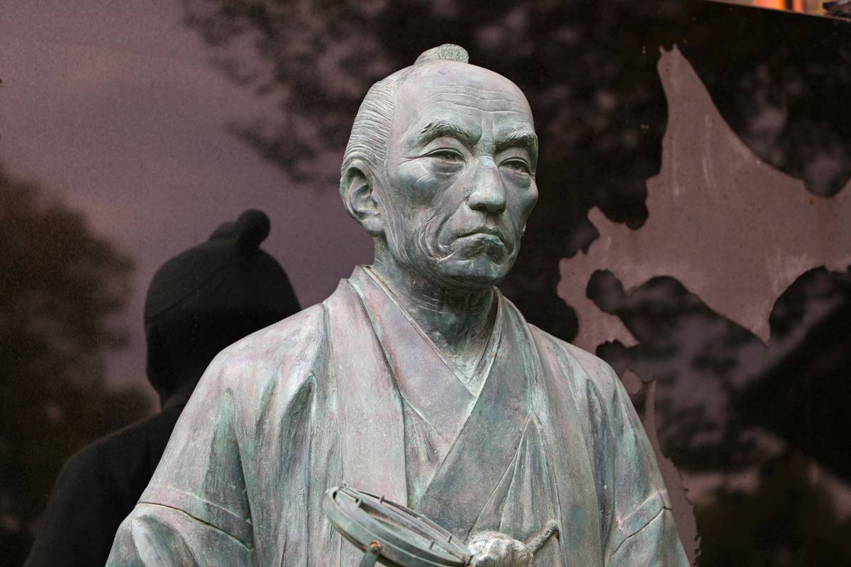 Bronze statue of an elderly East Asian man with a topknot, wearing a traditional robe and holding a surveying instrument.