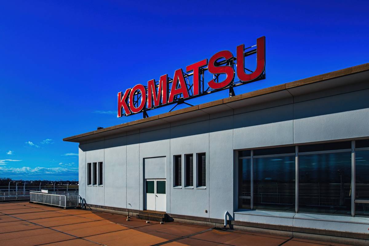 A building with a large red "KOMATSU" sign on its roof against a vibrant blue sky.