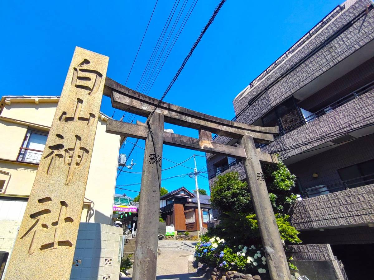 A stone torii gate and an inscribed stone pillar stand in a residential area under a clear blue sky.