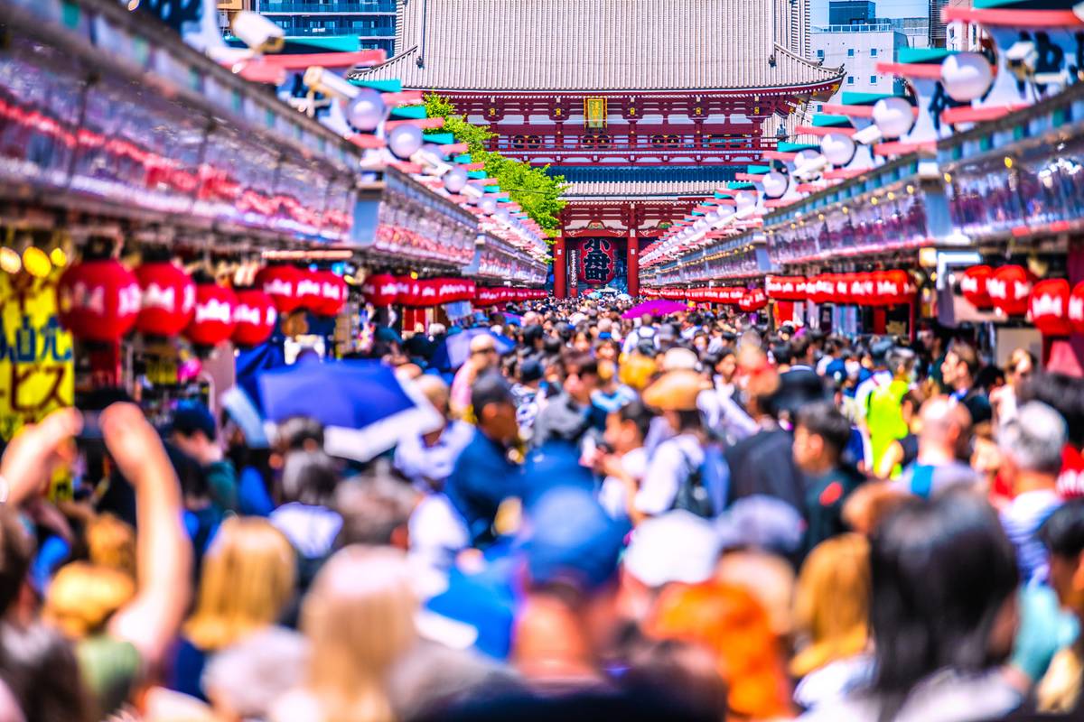 A crowded market street with red lanterns leading to a Japanese temple.