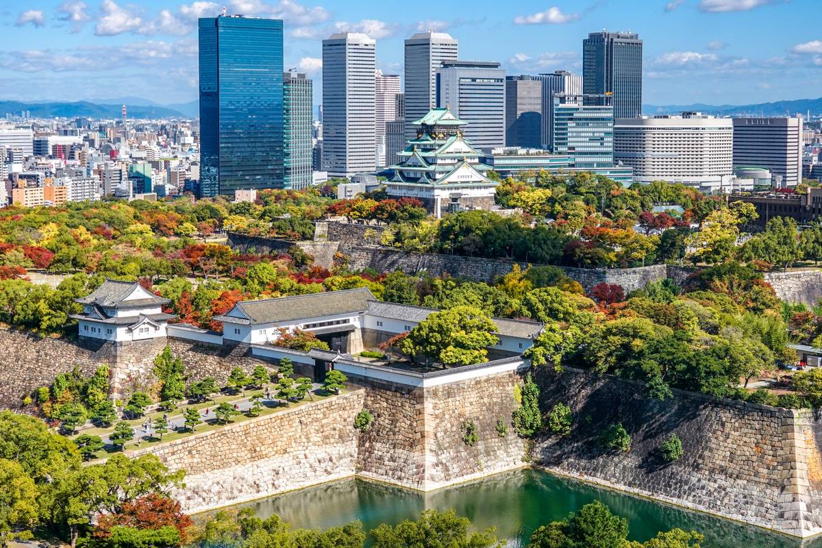 Osaka Castle and park with autumn trees, backed by a modern city skyline.