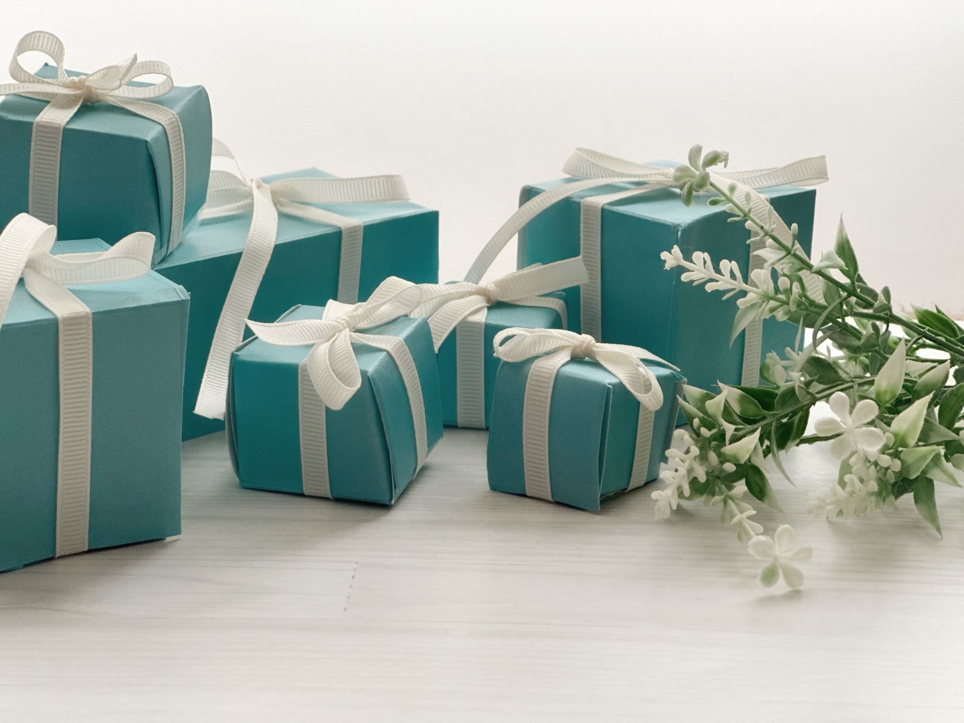 Multiple teal gift boxes with white ribbons, next to a sprig of white flowers.