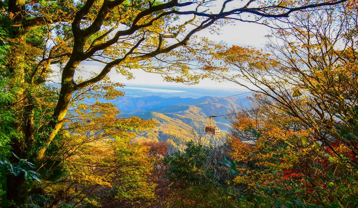 A cable car moves over mountains adorned with vibrant autumn foliage.
