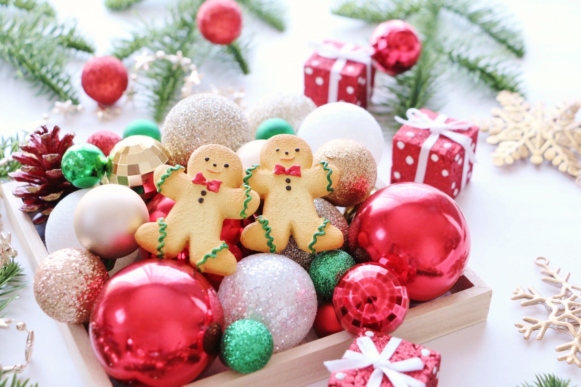 A wooden tray filled with colorful Christmas ornaments, pinecones, and two gingerbread cookies