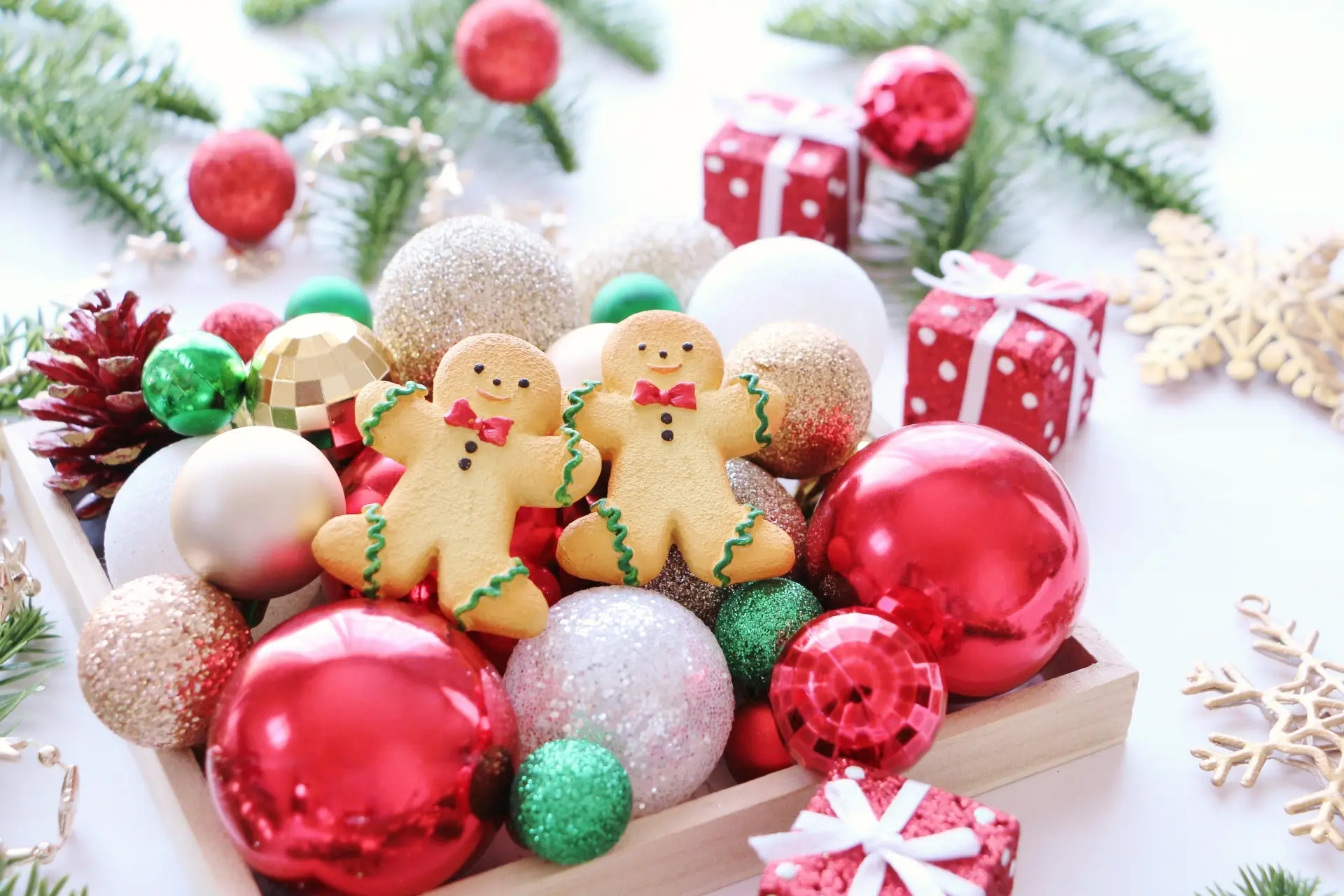 A wooden tray filled with colorful Christmas ornaments, pinecones, and two gingerbread cookies