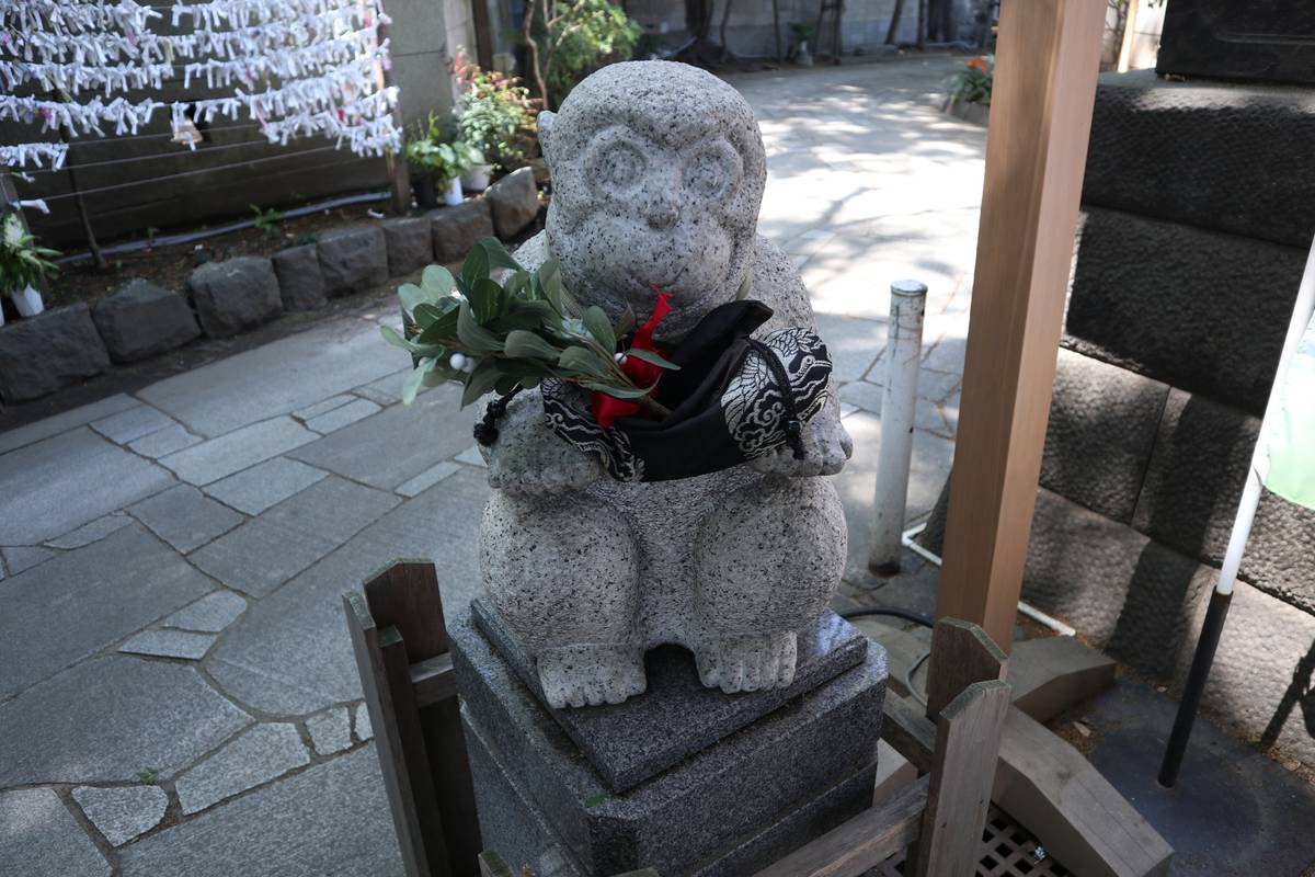 A squatting stone monkey statue holding a sprig of leaves and a patterned cloth in a shrine.
