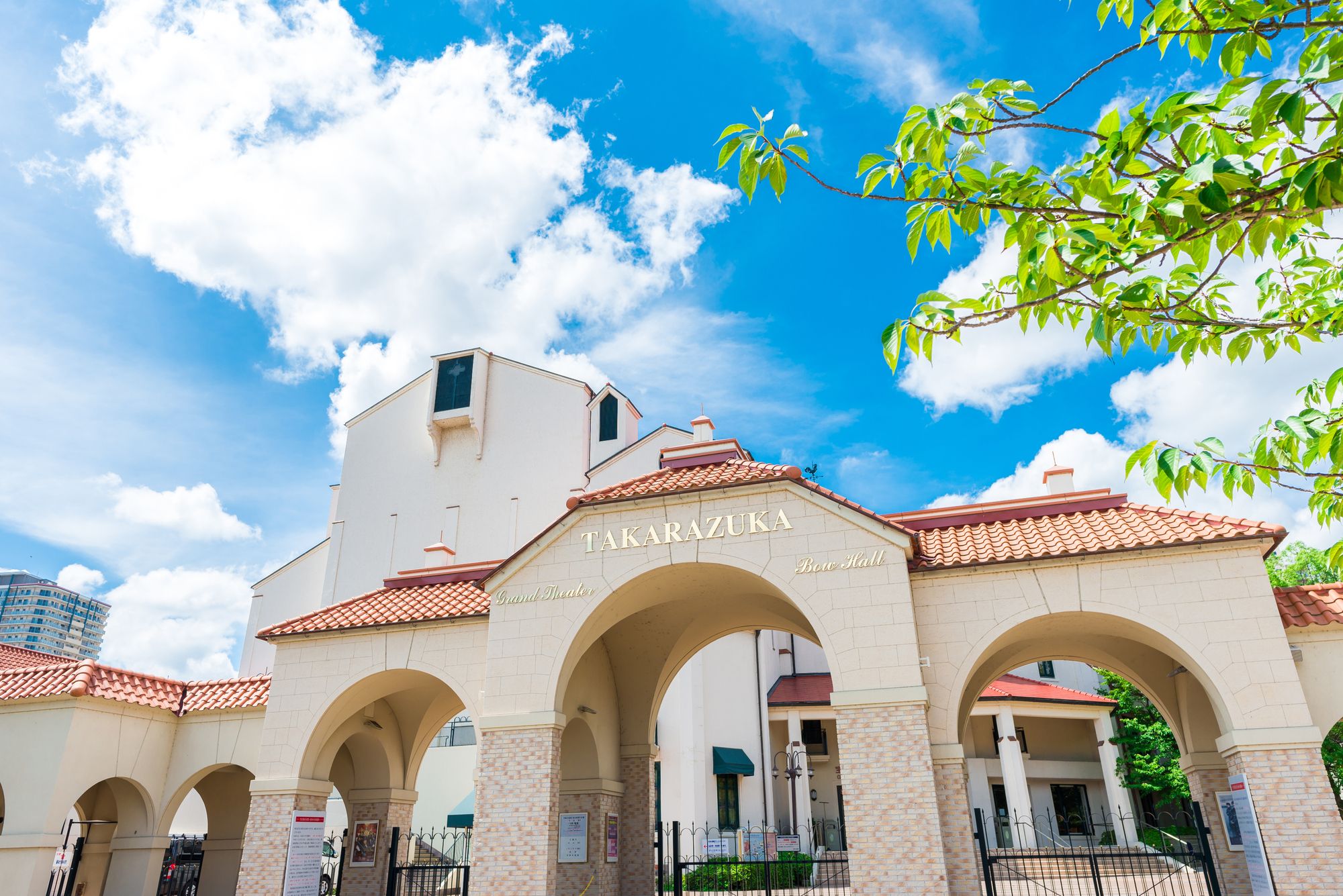 Takarazuka building with an arched entrance under a bright blue sky with green foliage.