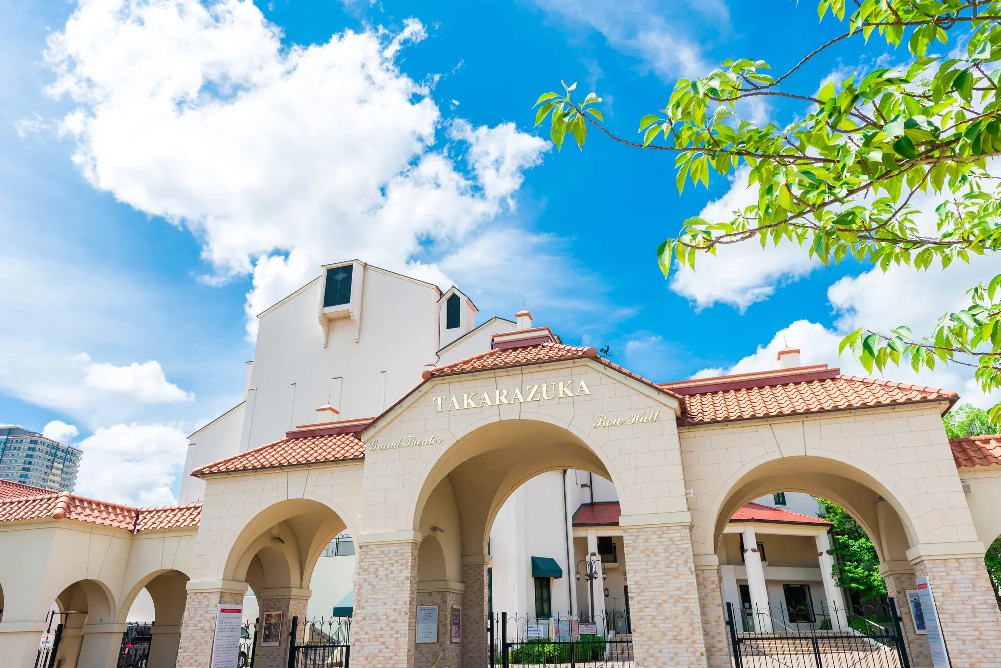 Takarazuka building with an arched entrance under a bright blue sky with green foliage.