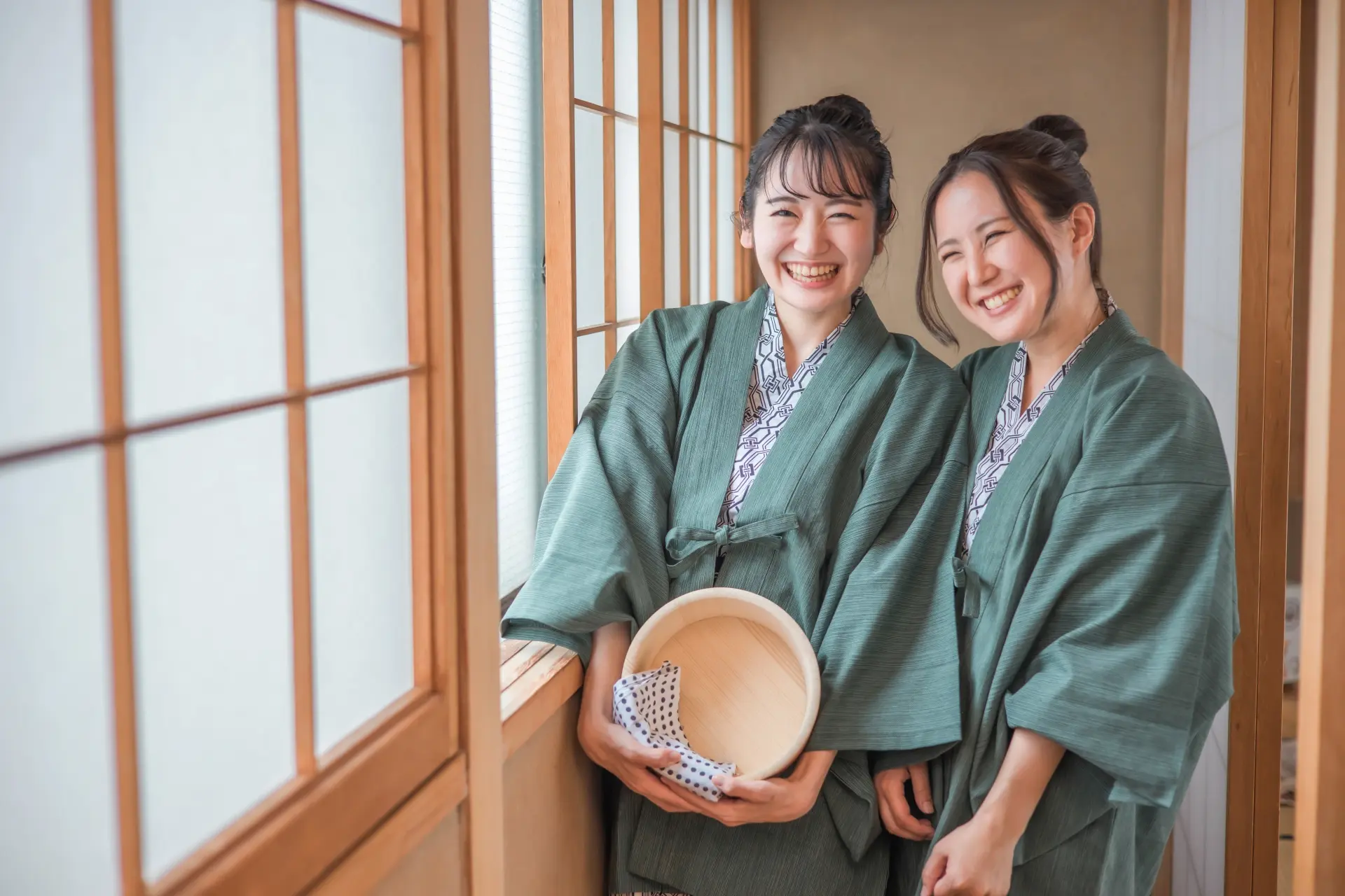 Two smiling women in green yukata in a traditional Japanese room.