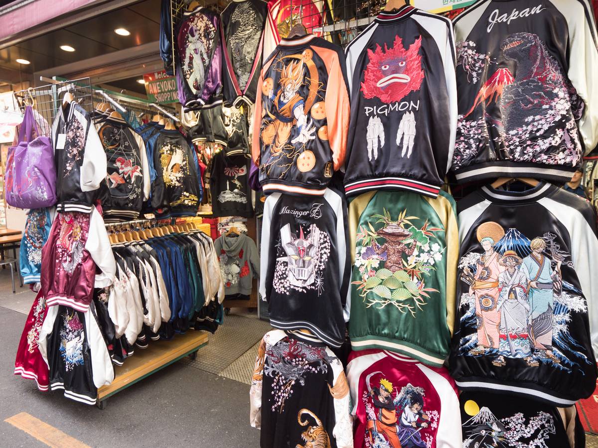 Rows of colorful embroidered Sukajan jackets featuring Japanese and anime designs displayed in an outdoor market.