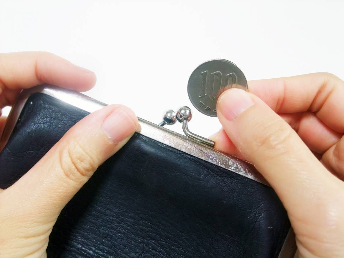 Hands dropping a 100 yen coin into a black coin purse.