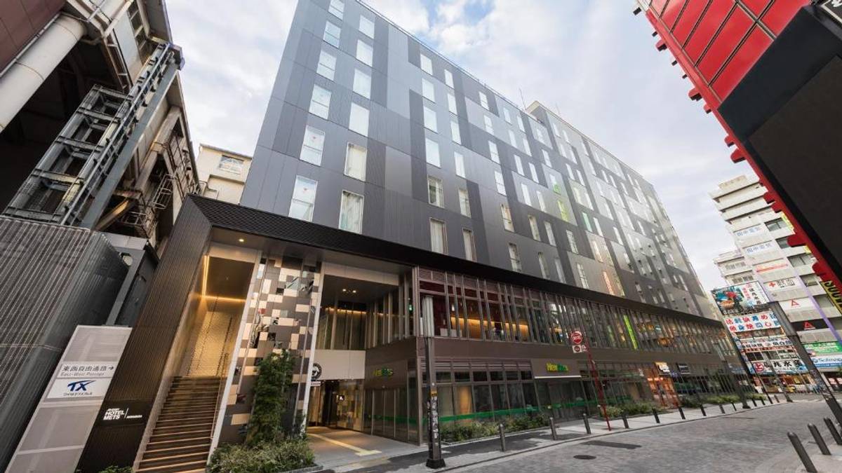 Modern dark gray building with irregular windows, street-level shops, and a staircase entrance, viewed from a city street.