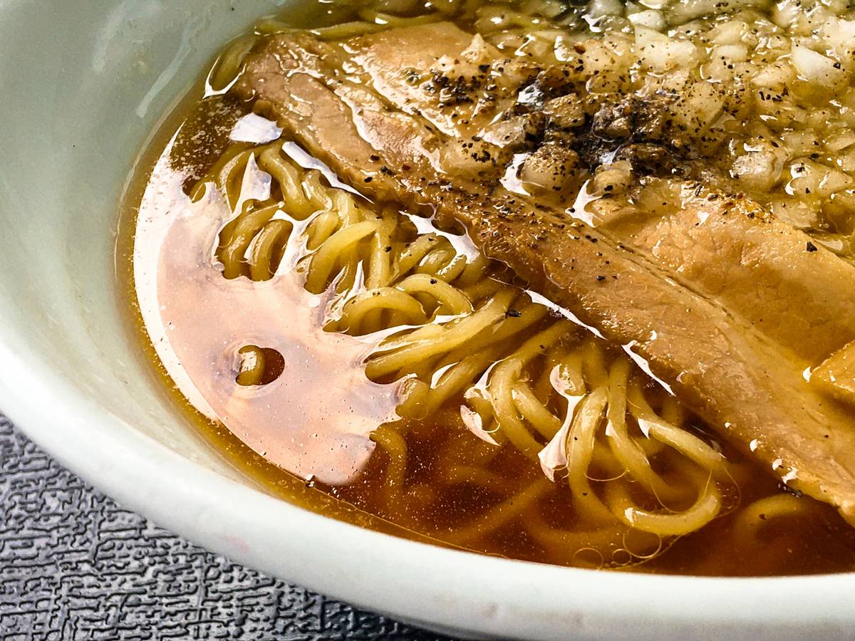A bowl of ramen with noodles, sliced pork, diced onions, and black pepper in broth.