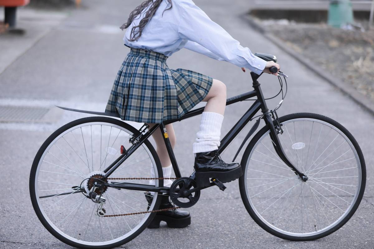 A person in a plaid skirt, white leg warmers, and platform boots rides a black bicycle.
