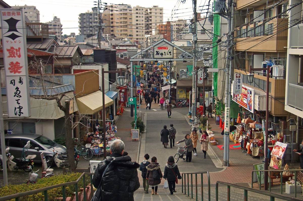 A bustling Japanese shopping street with pedestrians, many shops, and dense overhead wires.