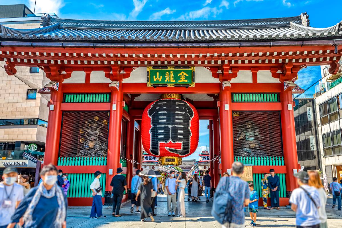 The Kaminarimon Gate of Sensoji Temple, a large red wooden gate with a huge red lantern and guardian statues, bustling with visitors.